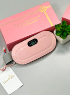 Pink electronic device with digital display on a gray surface, next to a pink gift box and small plant.